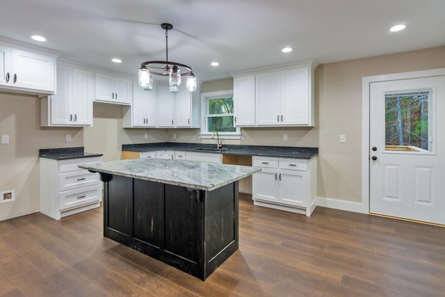 kitchen featuring decorative light fixtures, a center island, sink, white cabinets, and dark stone counters