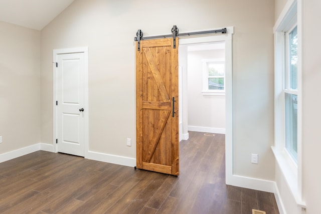 empty room featuring a barn door, vaulted ceiling, and dark hardwood / wood-style flooring