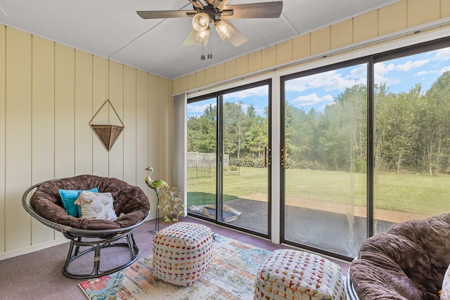 living area with carpet floors, wood walls, and ceiling fan