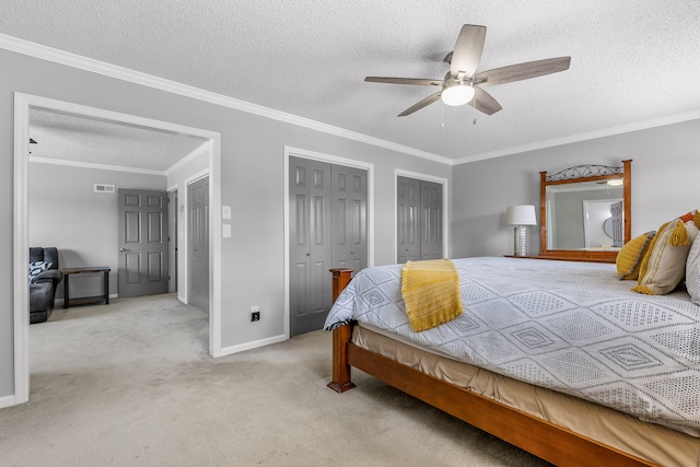 carpeted bedroom featuring a textured ceiling, ornamental molding, ceiling fan, and multiple closets