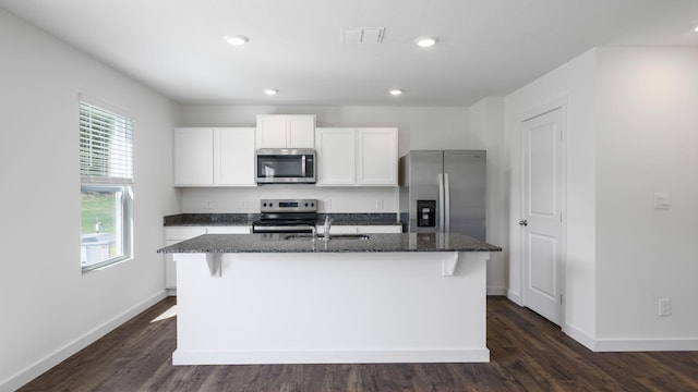 kitchen featuring dark stone countertops, visible vents, a center island with sink, appliances with stainless steel finishes, and white cabinetry