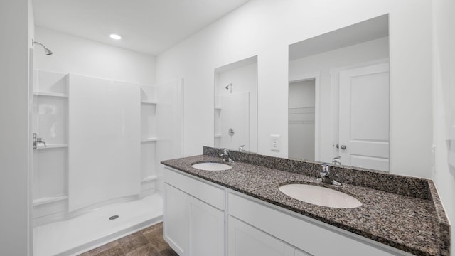 full bathroom featuring a sink, stone finish flooring, a shower, and double vanity