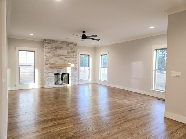 unfurnished living room featuring a wealth of natural light, crown molding, a stone fireplace, and wood finished floors