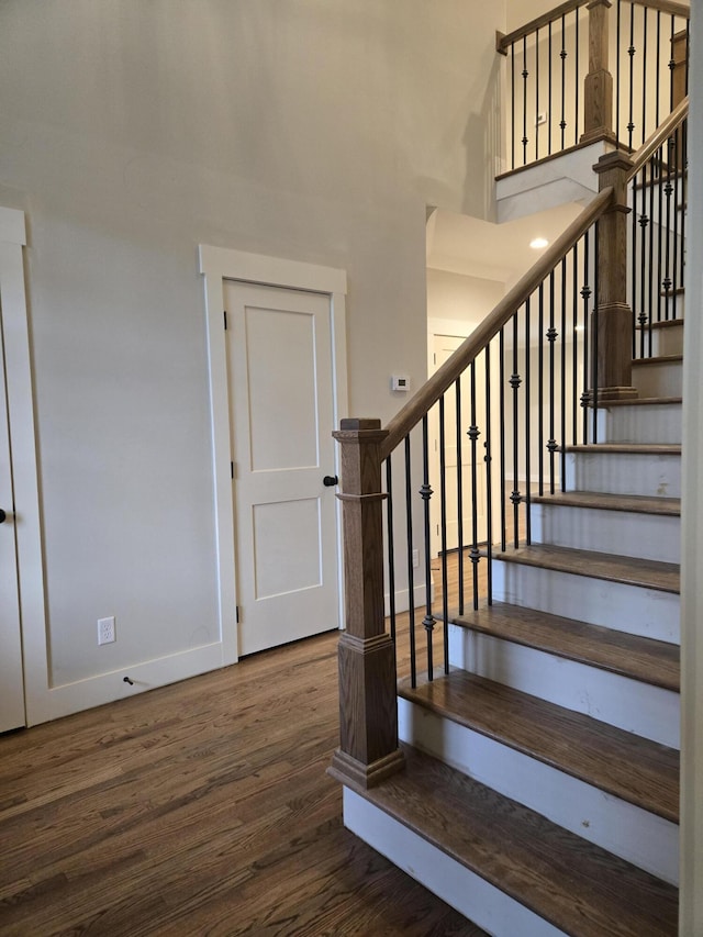 staircase featuring a high ceiling, baseboards, and wood finished floors