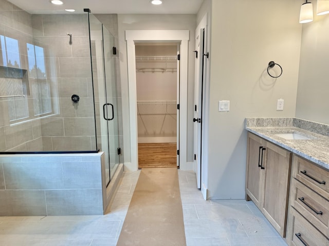 full bathroom with a stall shower, baseboards, a walk in closet, vanity, and recessed lighting