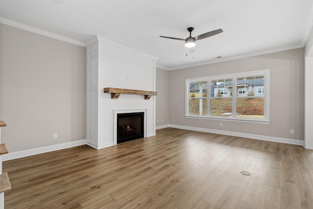 unfurnished living room featuring ceiling fan, a large fireplace, crown molding, and light wood-type flooring