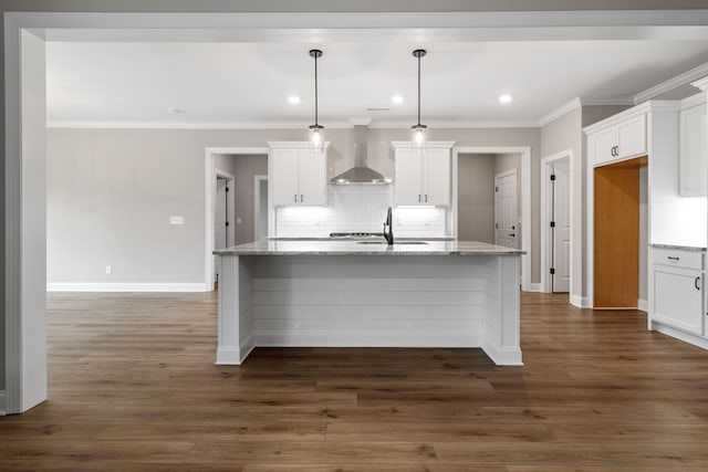 kitchen featuring a center island with sink, pendant lighting, and wall chimney range hood