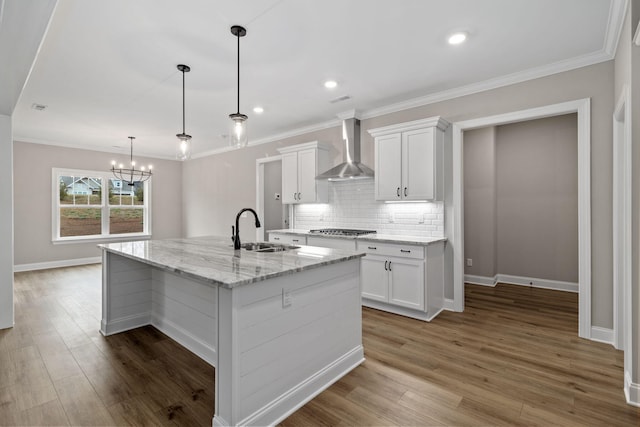 kitchen featuring stainless steel gas stovetop, light stone countertops, wall chimney range hood, white cabinets, and sink