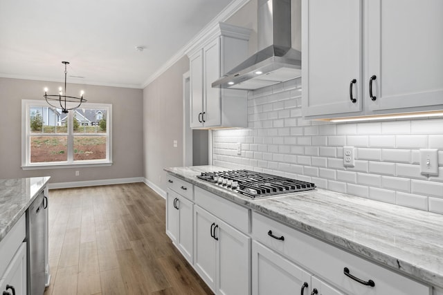 kitchen with appliances with stainless steel finishes, wall chimney exhaust hood, white cabinetry, ornamental molding, and light stone counters