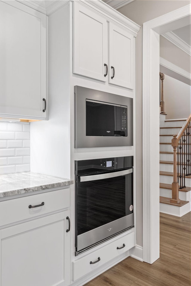 kitchen featuring white cabinetry, dark hardwood / wood-style floors, ornamental molding, stainless steel oven, and built in microwave