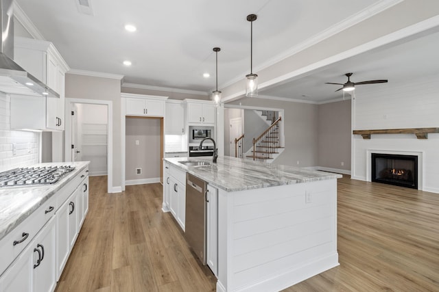 kitchen featuring light stone countertops, appliances with stainless steel finishes, wall chimney exhaust hood, white cabinetry, and an island with sink