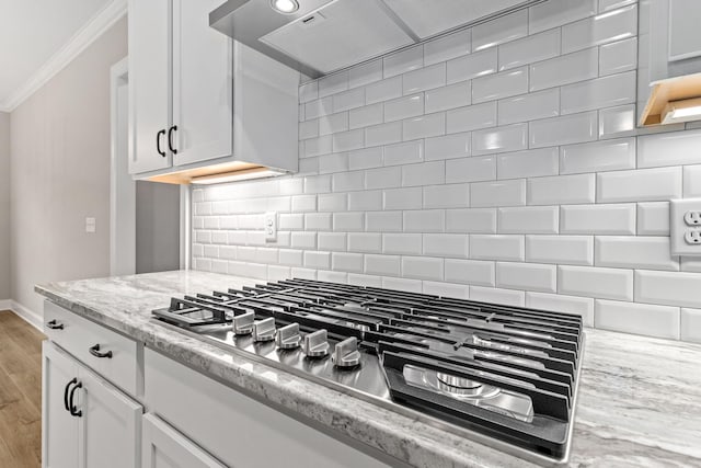 kitchen with stainless steel gas cooktop, white cabinetry, ornamental molding, backsplash, and light stone counters