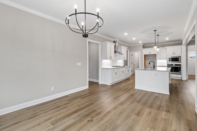 kitchen with white cabinets, appliances with stainless steel finishes, wall chimney exhaust hood, decorative light fixtures, and a kitchen island with sink