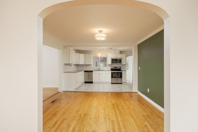 kitchen featuring white cabinetry, appliances with stainless steel finishes, crown molding, light hardwood / wood-style floors, and decorative backsplash