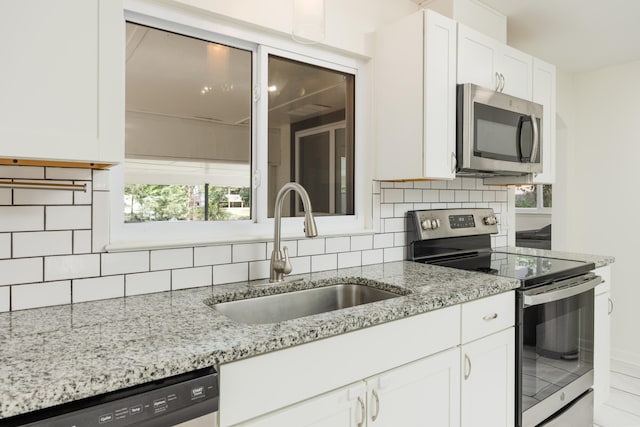 kitchen with tasteful backsplash, sink, white cabinets, appliances with stainless steel finishes, and light stone countertops