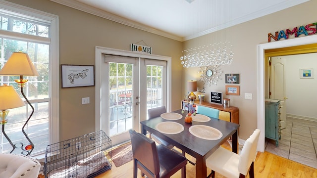 dining room featuring french doors, light wood-type flooring, ornamental molding, and a healthy amount of sunlight