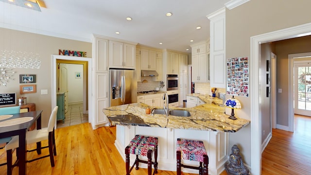 kitchen featuring appliances with stainless steel finishes, kitchen peninsula, a kitchen bar, light hardwood / wood-style flooring, and sink