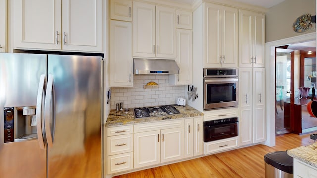 kitchen featuring light stone counters, backsplash, appliances with stainless steel finishes, range hood, and light wood-type flooring