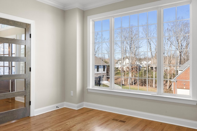 spare room featuring a chandelier, hardwood / wood-style floors, a healthy amount of sunlight, and crown molding