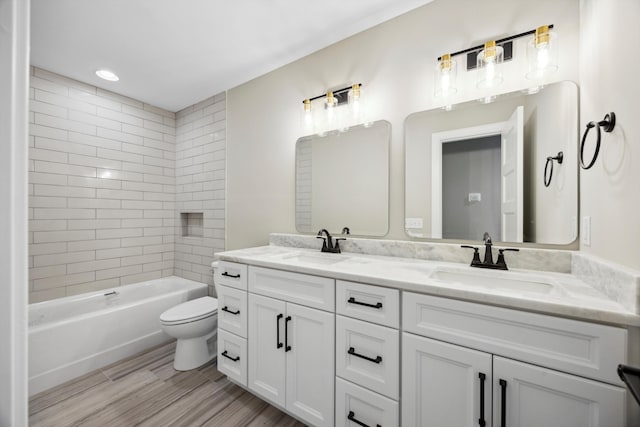 full bathroom featuring wood-type flooring, tiled shower / bath combo, vanity, and toilet