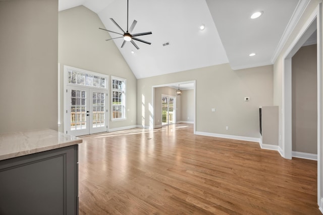 unfurnished living room featuring ornamental molding, french doors, high vaulted ceiling, light hardwood / wood-style flooring, and ceiling fan with notable chandelier