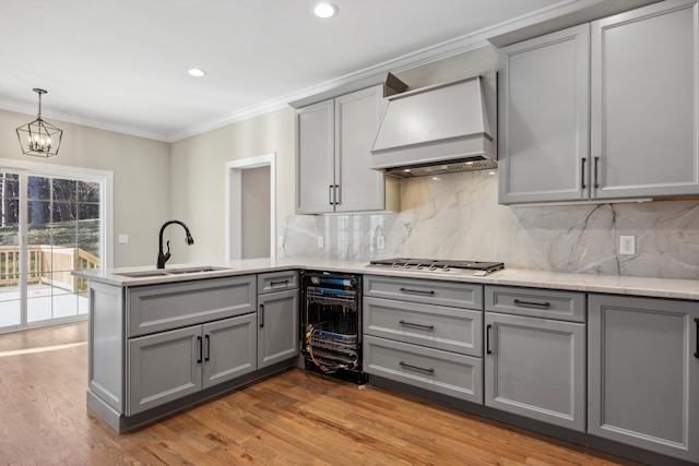 kitchen featuring kitchen peninsula, premium range hood, tasteful backsplash, stainless steel gas stovetop, and sink