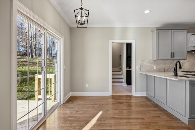 kitchen with light wood-type flooring, backsplash, gray cabinets, crown molding, and a notable chandelier