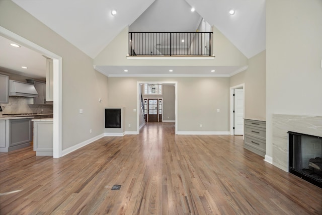 unfurnished living room featuring high vaulted ceiling, a fireplace, and light hardwood / wood-style flooring