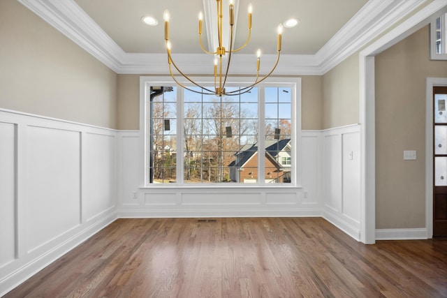 unfurnished dining area featuring wood-type flooring, an inviting chandelier, plenty of natural light, and crown molding