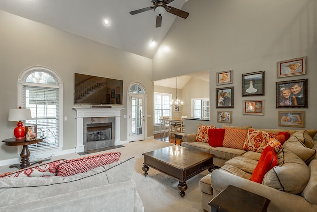 carpeted living room featuring ceiling fan with notable chandelier, a fireplace, and high vaulted ceiling