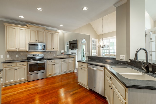 kitchen featuring appliances with stainless steel finishes, cream cabinetry, light wood-type flooring, an inviting chandelier, and sink