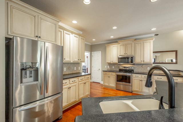 kitchen with appliances with stainless steel finishes, ornamental molding, cream cabinets, and sink