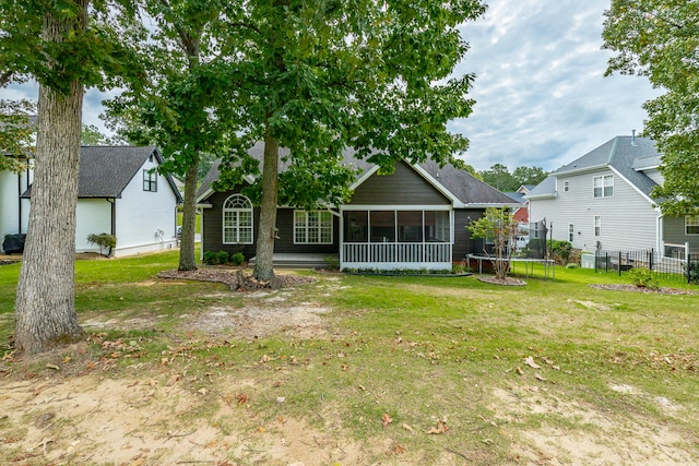 rear view of house featuring a trampoline, a sunroom, and a lawn