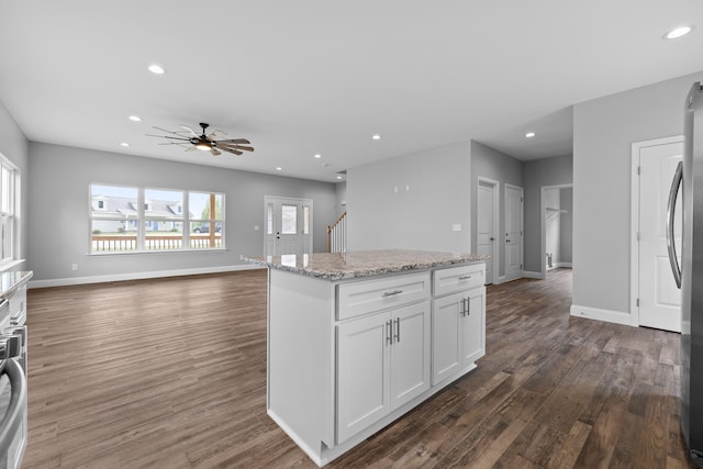 kitchen with white cabinetry, dark wood-type flooring, light stone counters, a kitchen island, and ceiling fan