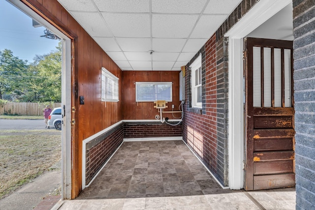 interior space featuring brick wall, a paneled ceiling, and wood walls