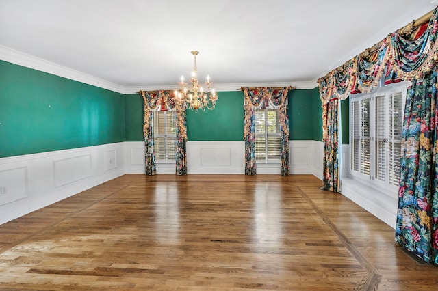 empty room featuring an inviting chandelier, ornamental molding, and hardwood / wood-style floors