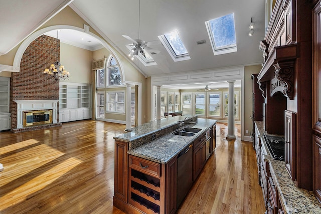 kitchen featuring ceiling fan with notable chandelier, a brick fireplace, a center island with sink, and sink