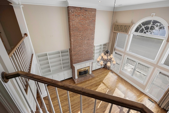 stairway with wood-type flooring, an inviting chandelier, a fireplace, and ornamental molding