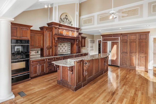 kitchen with ceiling fan, a kitchen island, black appliances, decorative columns, and a towering ceiling