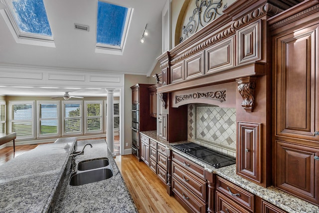 kitchen with light stone counters, ornate columns, vaulted ceiling with skylight, sink, and light hardwood / wood-style floors