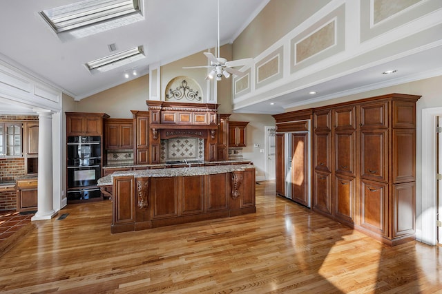 kitchen featuring decorative columns, double oven, a center island, and a skylight