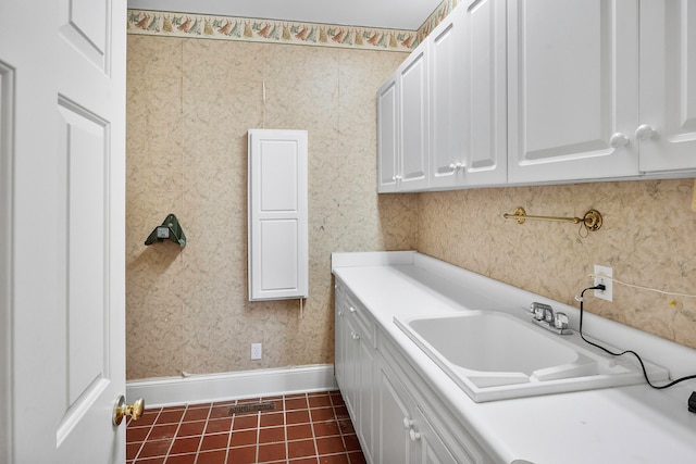 clothes washing area with sink, dark tile patterned flooring, and cabinets