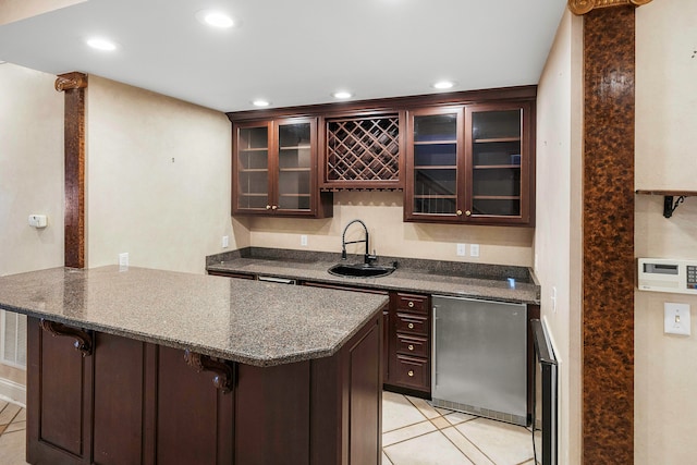 interior space featuring kitchen peninsula, light tile patterned floors, a kitchen bar, dark brown cabinetry, and sink