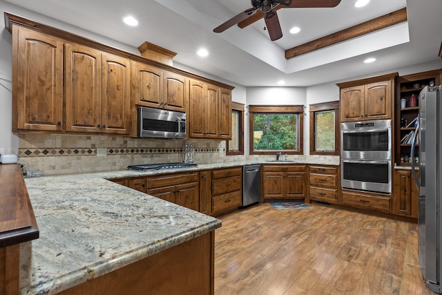 kitchen with ceiling fan, light stone counters, wood-type flooring, appliances with stainless steel finishes, and decorative backsplash