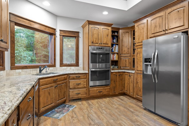 kitchen featuring light stone counters, sink, backsplash, appliances with stainless steel finishes, and light wood-type flooring