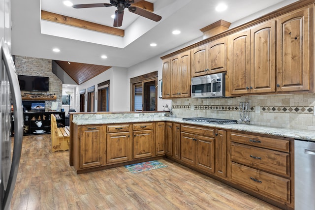 kitchen with light stone counters, kitchen peninsula, light hardwood / wood-style flooring, stainless steel appliances, and ceiling fan