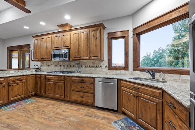 kitchen with appliances with stainless steel finishes, light stone countertops, sink, and light hardwood / wood-style flooring