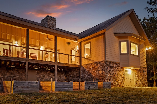 back house at dusk featuring ceiling fan, a balcony, and a yard