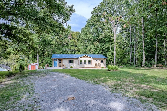 ranch-style house featuring an outbuilding, metal roof, driveway, a front lawn, and a storage shed