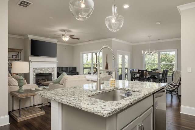 kitchen with light stone countertops, decorative light fixtures, ornamental molding, dark hardwood / wood-style floors, and a kitchen island with sink